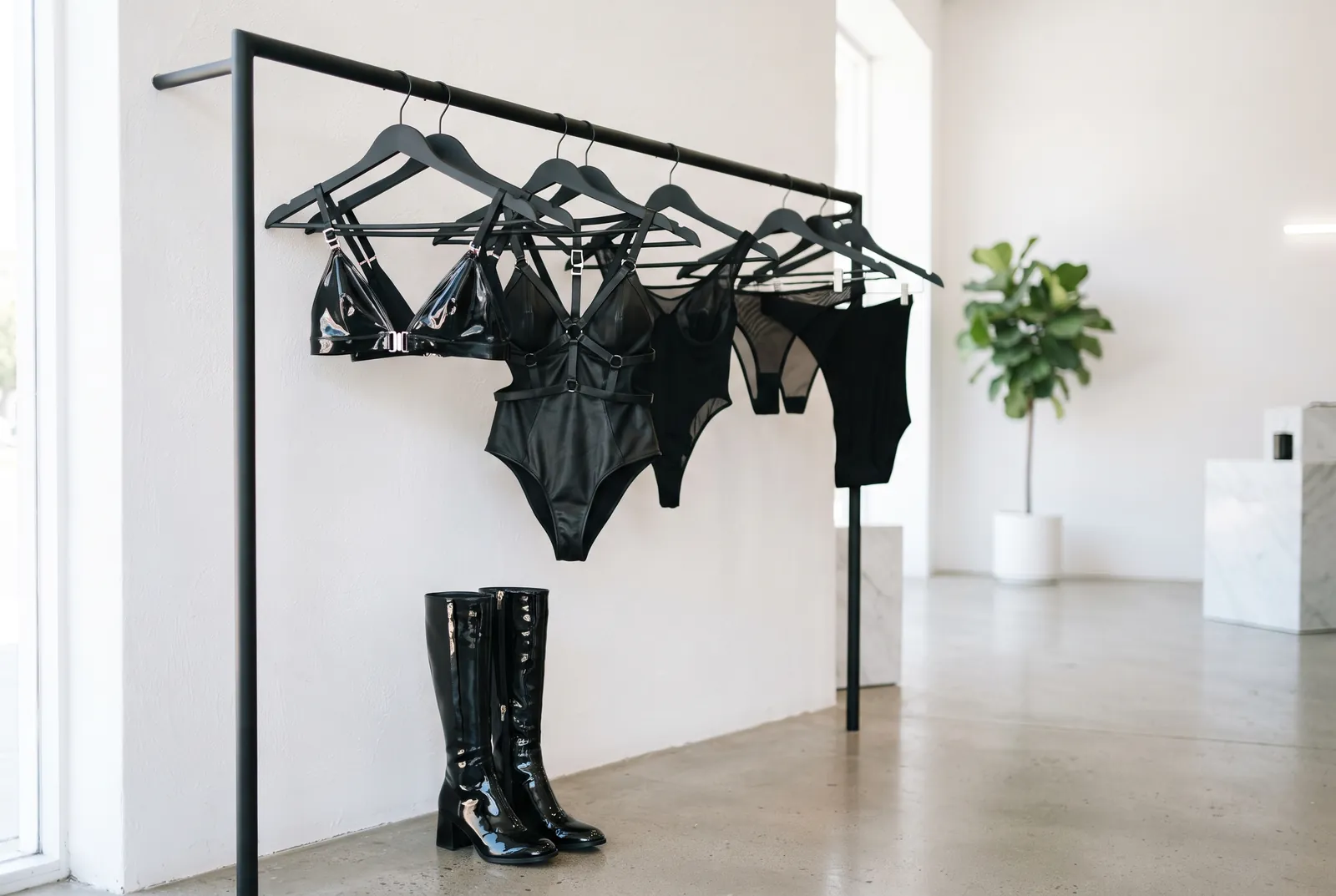 Stender minimal con body in pelle e lattice e stivali in vernice in una boutique luminosa