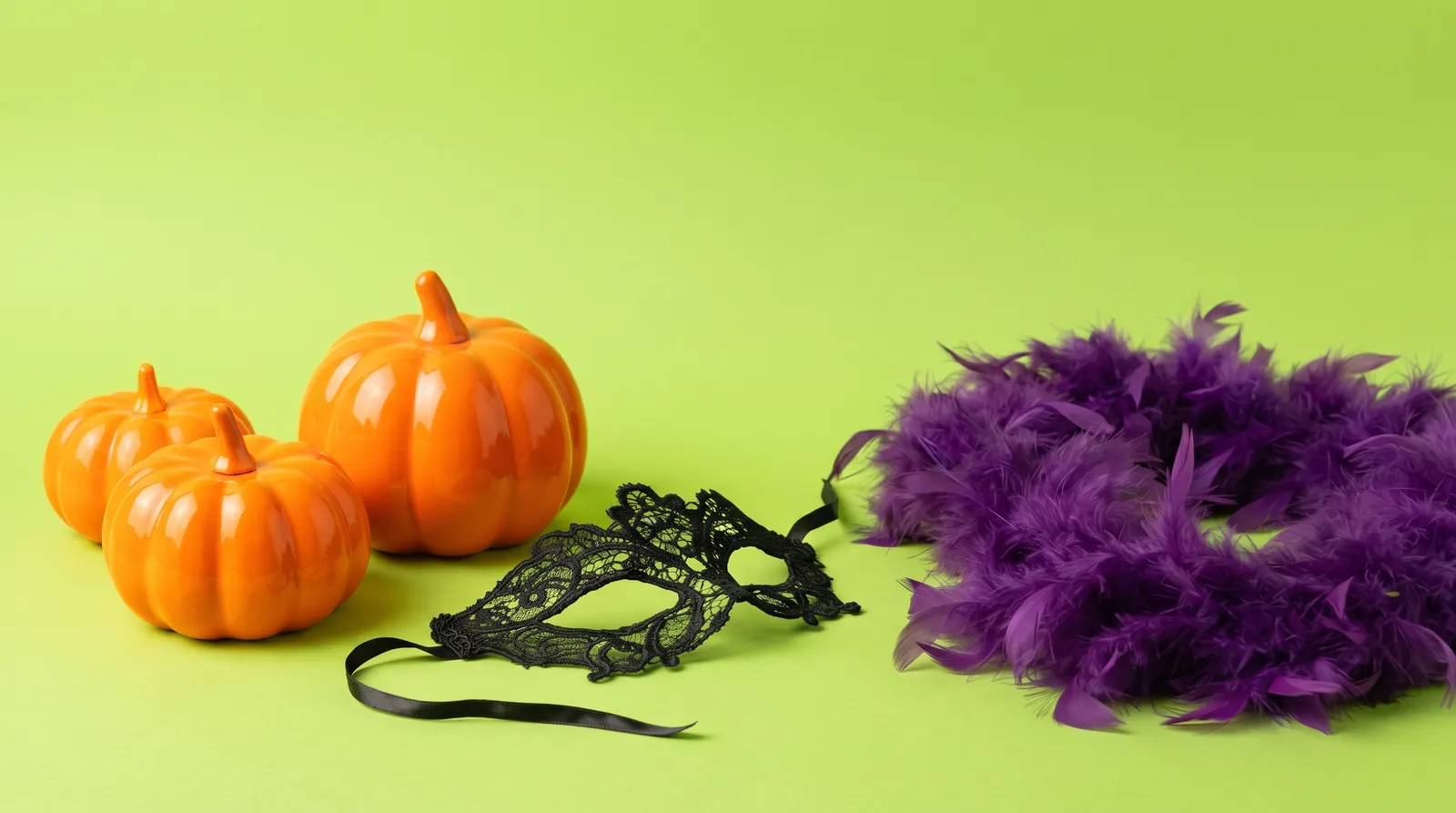 Giochi di ruolo Halloween: zucche arancioni, maschera di pizzo nera e boa viola su sfondo lime